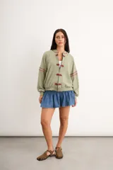 Campera verde militar de corte oversize, con cierre frontal y broches decorativos de estilo oriental en rojo, mangas largas y detalles bordados en rojo en el cuello y las mangas.