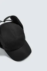Gorra técnica de color negro con diseño de cinco paneles y orejeras integradas ajustables mediante una trabilla superior. Confeccionada en tejido acolchado, cuenta con ajuste elástico en la parte posterior.