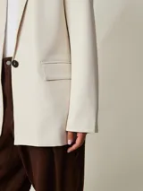 Blazer beige claro de corte recto, con solapas de muesca, mangas largas y bolsillos frontales.