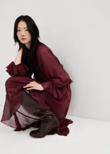 Vestido largo bordó de poliéster, de corte oversize, con escote en V y detalle de volantes en la cintura y el canesú. Cuenta con mangas largas y forro interior.