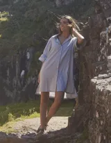 Vestido camisero corto color gris, con cuello clásico, cierre frontal de botones y mangas tres cuartos con volados en los puños.