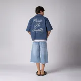 Camisa de manga corta azul oscuro de corte boxy, confeccionada en algodón. Presenta cuello camisero, cierre frontal con botones y un pequeño bordado en el pecho con las siglas 'VCP CNPT' y el número '333'.