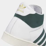 Championes Adidas modelo Jabbar Hi, de corte medio, con exterior de cuero blanco, detalles en gamuza verde oscuro en las tres tiras laterales y el cuello, y suela de goma color crema.