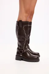 Bota de caña media en cuero sintético negro, con suela track, cierre lateral y detalle de tachas metálicas en la parte superior y en una tira decorativa sobre el tobillo.