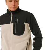 Canguro con cierre frontal de la línea Anti Series de Rip Curl. Presenta un diseño de bloques de color en beige y negro, cuello alto, bolsillos laterales y un bolsillo vertical con cierre en el pecho que incluye el logo de la marca.