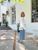 Cartera tipo sobre color crudo, confeccionada en cuero, con correa larga de cuero marrón y costuras decorativas en contraste.