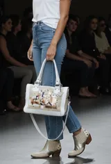 Cartera de cuero natural de diseño contemporáneo y versátil, intervenida con arte original por Carolina De Cunto en el frente, combinando tonos marfil y arena con detalles pintados a mano. Cuenta con estructura firme, herrajes de metal, manijas superiores, correa regulable desmontable y bolsillos internos y externos.