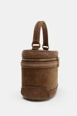 Bolso formato vanity de gamuza color marrón, con asa de mano superior y correa bandolera extraíble y ajustable. Presenta cierre de doble cremallera metálica dorada y detalles de pespuntes en el cuerpo.