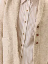 Saco de lana hervida con cuello solapa, cierre frontal de botones rústicos y bolsillos laterales. Presenta un diseño clásico con textura delicada y duradera.