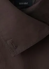 Chaqueta marrón de corte recto y diseño crop, confeccionada en mezcla de algodón y poliamida con forro interior de poliéster. Presenta cuello alto tipo embudo, doble botonadura frontal, manga larga y dos bolsillos laterales.