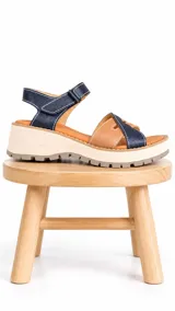 Sandalia de cuero bicolor en tonos azul y camel, con plataforma track liviana, tiras cruzadas en el empeine y tira ajustable con velcro en el talón.