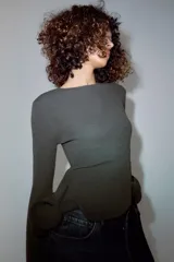 Jersey de punto gris oscuro con cuello redondo y manga larga, con bajo asimétrico acabado en volante con varilla metálica interior.
