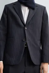 Blazer de corte relajado confeccionado en tejido de lana con estampado de raya diplomática. Presenta cuello con solapas de muesca, cierre frontal de dos botones, bolsillos de vivo en la cadera y abertura central en la espalda. Incluye forro interior a contraste.