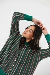 Sweater verde esmeralda de cuello redondo y manga larga, con terminación acanalada en puños y ruedo. Presenta tajos laterales y diseño de rayas verticales en tonos blanco y rosa.