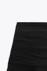 Falda pantalón de tiro medio en color negro, con diseño de pliegues en la parte superior y volantes en el ruedo. Cuenta con cierre lateral.