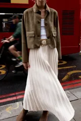 Falda midi plisada de tiro alto color beige, con cinturón a tono y hebilla metálica dorada. Cierre lateral con cremallera oculta.