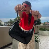 Cartera de hombro color marrón oscuro con textura de cocodrilo (efecto croco) y acabado brillante. Tiene forma de media luna y asa corta.