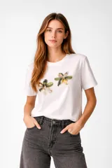 Remera de algodón blanca de manga corta y corte holgado, con cuello redondo a la base y apliques de flores bordadas con lentejuelas en el frente.