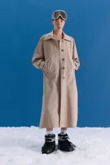 Trench midi de color camel, confeccionado en una mezcla de algodón y nylon con propiedades repelentes al agua. Presenta un diseño clásico con cuello camisero, cierre frontal de botones, bolsillos laterales y tajos en los costados.
