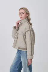 Campera acolchada de diseño capitoné en color beige, con cuello alto, cierre frontal y bolsillos laterales. Presenta un corte holgado con detalles de costuras reforzadas en las mangas y ajuste en la cintura.