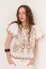 Blusa blanca de manga corta con detalles de bordados y perforaciones, cuello redondo y diseño holgado.