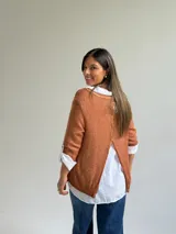 Sweater de punto color naranja con diseño asimétrico, que incluye una bufanda a juego con detalles bordados y una camisa blanca de base integrada.