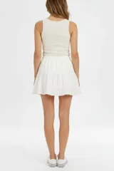Falda corta de viscosa y algodón color blanco, con cintura elástica con cordón ajustable y diseño de volados escalonados.
