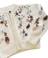 Cardigan de punto color marfil, con cuello redondo a la base, mangas largas y cierre frontal con botones. Presenta un delicado bordado artesanal de flores en tonos bordó, rosado y celeste con tallos y hojas verdes en el frente y las mangas.