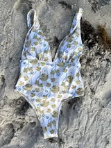 Traje de baño entero blanco con estampado de conchas marinas doradas y cadenas con gemas azules.