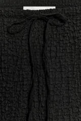 Falda midi de tiro medio en color negro, confeccionada en tejido de punto con textura y cintura elástica ajustable con cordones.