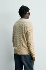 Sweater de punto con diseño de trenzas, color beige, cuello redondo y manga larga con terminaciones en rib.
