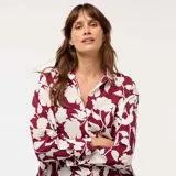 Blusa de corte fluido y holgado con estampado floral en tonos bordó y crema. Presenta cuello camisero, cierre frontal con botones y mangas largas con puños rectos.