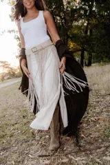 Cinturón artesanal de cuero color arena, con flecos largos y hebilla cuadrada metálica.