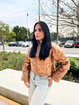 Campera corta color ocre, con cuello alto, cierre frontal con cremallera y diseño acolchado.