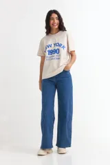 Remera de manga corta color beige, con estampa frontal en tono azul con la leyenda "New York 1990", de corte holgado y diseño casual.