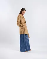 Campera tipo trench de color habano, de corte a la cadera, confeccionada en material textil símil gamuza. Presenta solapa cruzada, doble botonadura frontal, hombreras y cinturón ajustable para anudar en la cintura. Incluye bolsillos delanteros y puños con trabilla.