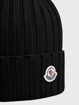 Gorro tipo beanie de lana acanalada en color negro, con parche del logo de la marca en la parte frontal.