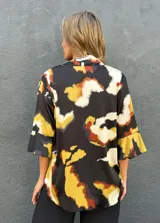 Blusa de satén con escote en V y mangas tres cuartos acampanadas, con estampado abstracto en tonos negro, caramelo, verde lima y blanco.