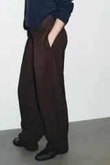 Pantalón de tiro alto con diseño tipo balloon, confeccionado en tela con estampado de rayas verticales. Presenta cintura ancha, pliegues frontales, bolsillos laterales y cierre frontal con cremallera, botón y ganchos metálicos.