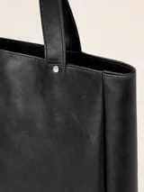 Bolso tipo tote grande de cuero negro con acabado texturizado, cierre superior, doble asa de hombro y parche con logo de la marca en el frente.