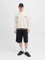 Buzo de manga larga color blanco roto (sea salt) con cuello redondo y calce oversize cropped. Presenta un estampado gráfico en la espalda con texto en color borgoña, incluyendo las palabras "RESPORT", "ATHLETIC ESSENTIALS", "CREATIVE DEPT." y el año "1990".