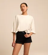 Short de sarga color blanco, de cintura alta, con bolsillos delanteros y traseros, trabillas para cinturón y bajo plegado. Cuenta con cierre frontal de botón y cremallera.