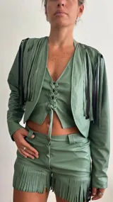 Campera corta verde con flecos negros en la parte superior y cierre frontal con lazo.