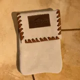 Funda para celular de gamuza color arena, con solapa y detalles de costura en cuero marrón. Incluye un parche de cuero con el logo de la marca Sierra Mora.