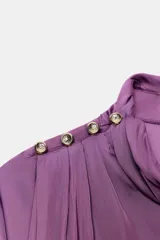 Blusa de satén color lila con cuello subido, manga larga con puños anchos y detalle de botones dorados en el hombro.