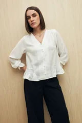 Camisa negra de manga larga con escote en V y botones forrados al tono en el frente. Destaca por su textura sutil y por el detalle de frunces con volados en la parte inferior.