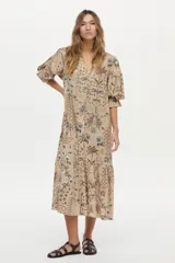 Vestido túnica de lino y viscosa, color camel con estampa artesanal en tonos oscuros, escote en V profundo, mangas amplias abullonadas y falda larga con volado en el ruedo.