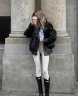 Chaqueta de cuero sintético color negro con acabado granulado, diseño oversize, cuello alto estructurado y cierre asimétrico.