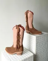 Botas estilo tejano de caña alta, confeccionadas en cuero vacuno. Presentan una combinación de colores en beige y marrón texturizado, con detalle de flecos laterales y borde superior en color rojo.