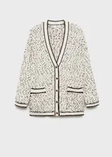 Cardigan de punto grueso con diseño jaspeado en blanco y negro. Presenta cuello en pico, cierre frontal con botones efecto joya, dos bolsillos de parche delanteros y detalles en contraste negro en los bordes.